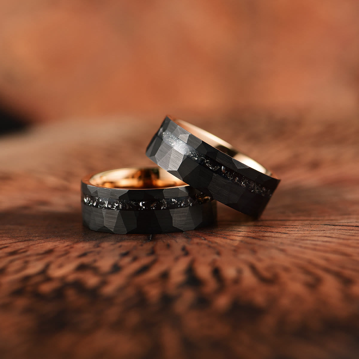 Zwei schwarze Eheringe mit Diamanten, facettiert, auf Holzoberfläche.