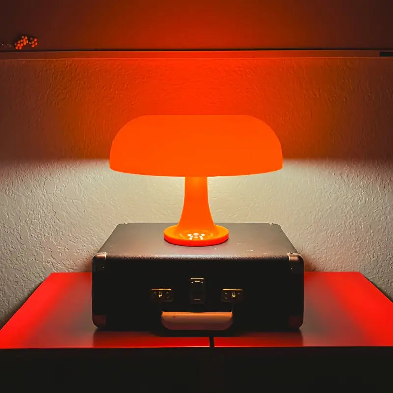 Orange Tischlampe auf schwarzem Koffer, modernes Design, warmes Licht, Inneneinrichtung.