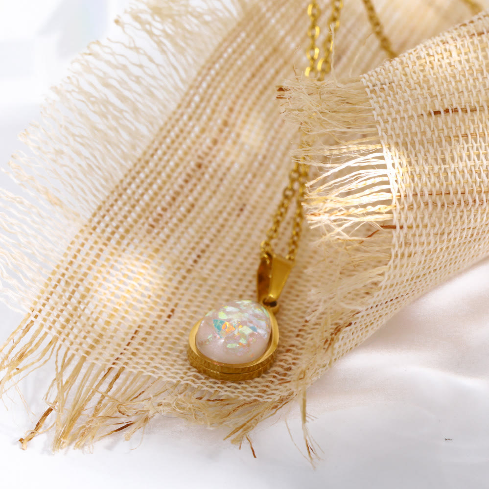 Goldene Halskette mit rundem Opal-Anhänger auf beigem Stoff, eleganter Schmuck für Damen.