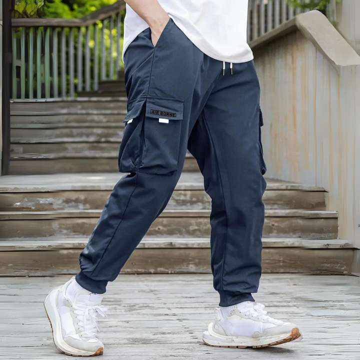 Mann in blauer Cargohose und weißen Sneakers auf Holztreppe, lässige Mode, Outdoor-Stil.