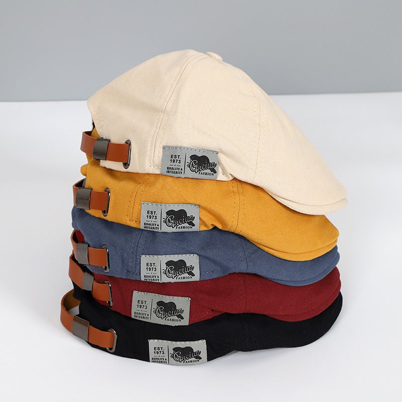 Stapel von Schiebermützen in Beige, Gelb, Blau, Rot, Schwarz mit Lederriemen und Etikett.
