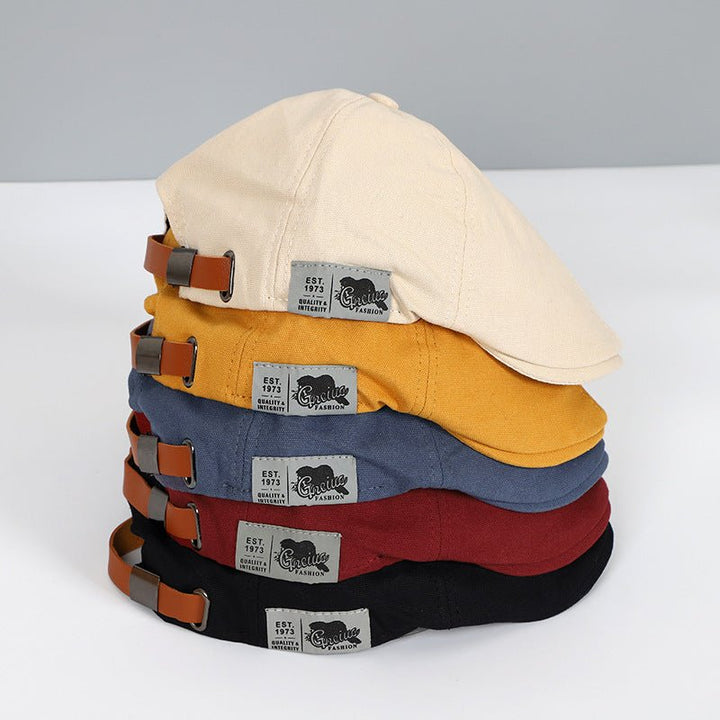 Stapel von Schiebermützen in Beige, Gelb, Blau, Rot, Schwarz mit Lederriemen und Etikett.