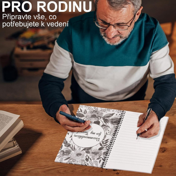 Starší muž s brýlemi u dřevěného stolu drží telefon a píše propiskou do rozevřeného kroužkového plánovače s linkovanou stránkou. 4