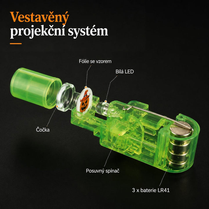 Rozložený zelený projektor ukazuje čočku, motivovou fólii, bílou diodu, posuvný spínač a tři knoflíkové baterie 8