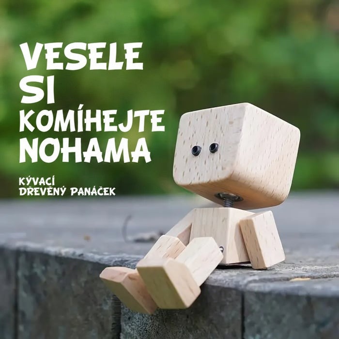 Dřevěná figurka s černýma očima sedí na kamenné zídce před zelenou rozostřenou zahradou, nohy visí dolů. 13