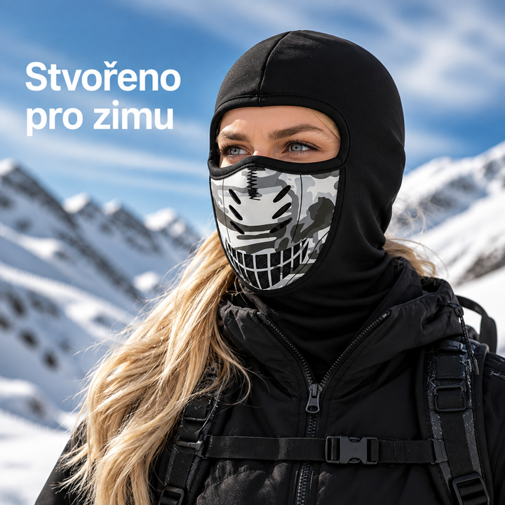 Žena v černé kukle s kamuflážním panelem přes ústa a nos stojí na slunci před zasněženými horami. 1