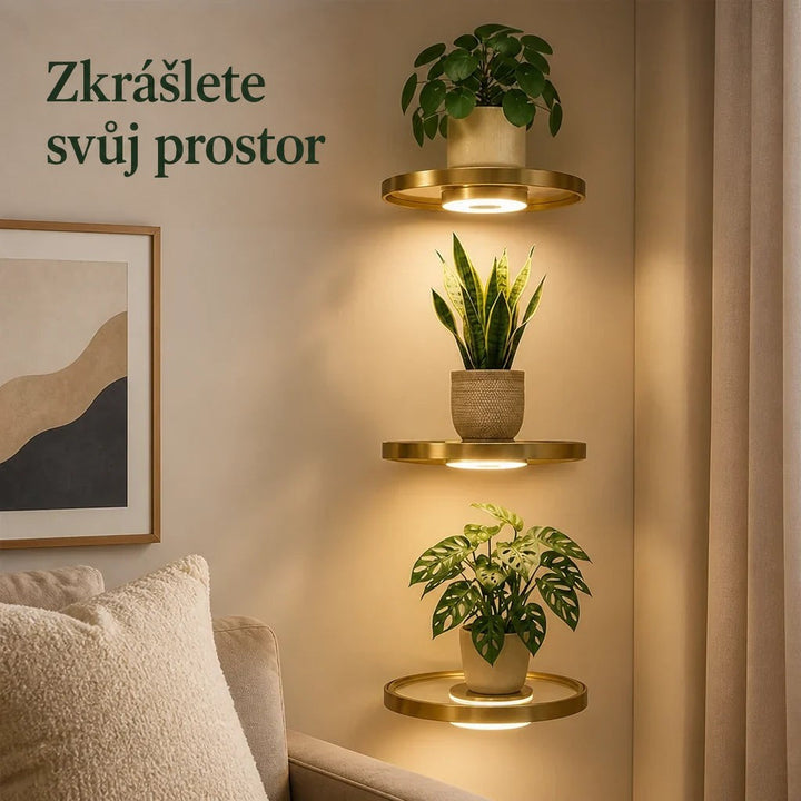 Tři kulaté zlaté police nad sebou na stěně u pohovky, každá s rostlinou v květináči a teplým světlem zespodu. 1
