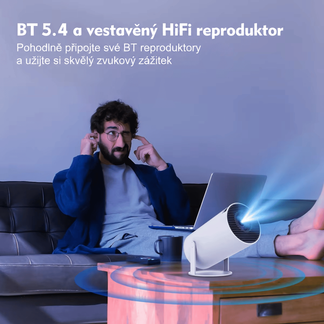 Muž s prsty v uších na pohovce, před ním na stolku projektor s vlnami zvuku z reproduktoru 9