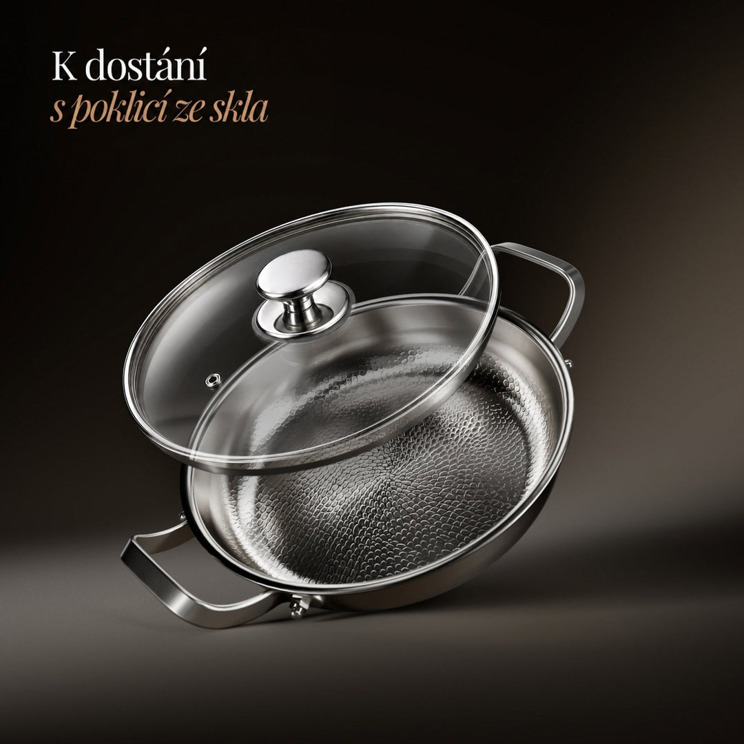 Pánev se strukturovaným dnem a nad ní našikmo vznášející se skleněná poklice s kovovým knoflíkem na tmavém pozadí. 3