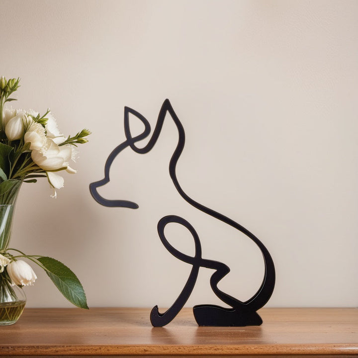 Schwarze Chihuahua-Skulptur aus Metall auf Holzoberfläche neben Blumenstrauß.