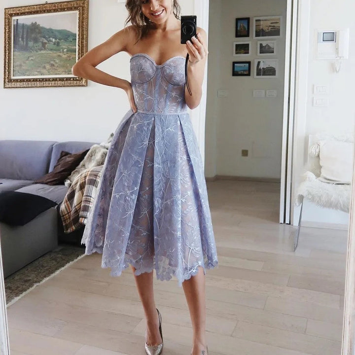 Frau im blauen Spitzenkleid, trägerlos, knielang, elegantes Design, Wohnzimmer-Hintergrund.