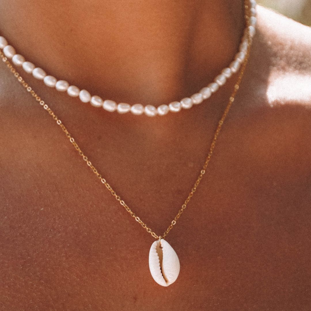 Frau mit goldener Kette und Kaurimuschel-Anhänger, Perlenhalskette, Sommermode-Schmuck.