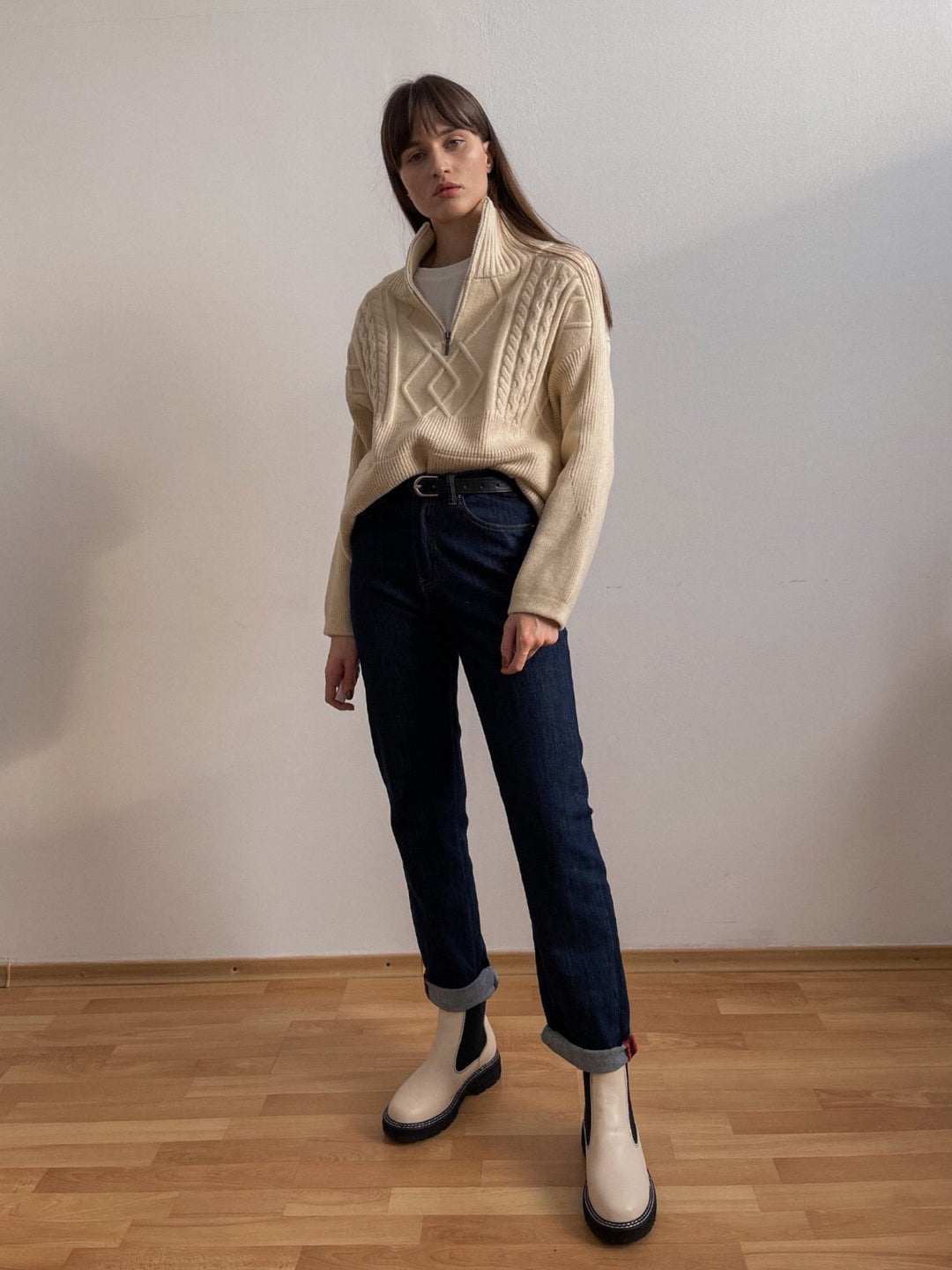 Frau in cremefarbenem Strickpullover und blauen Jeans, weiße Stiefel, modischer Look.