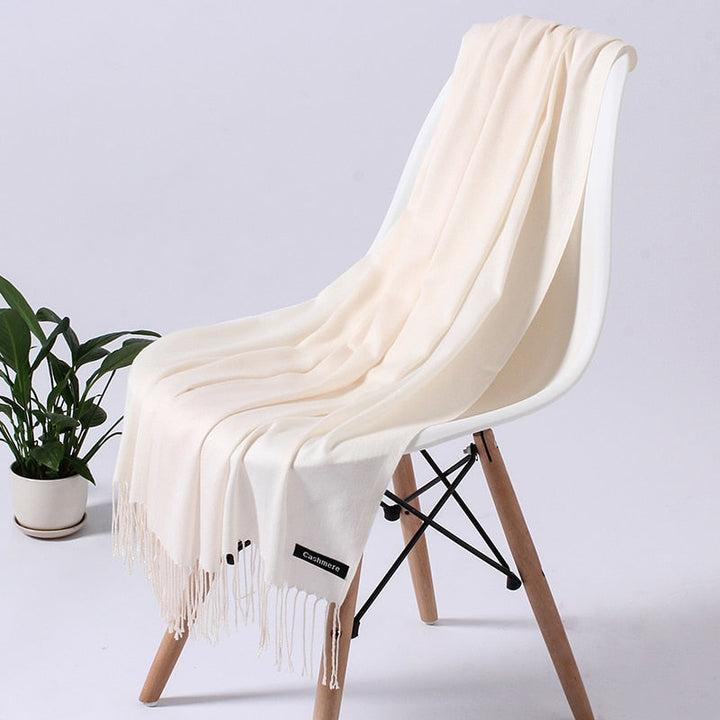 Cremefarbener Kaschmirschal auf weißem Stuhl, weiches Material, elegantes Design, Wohnzimmer-Deko.