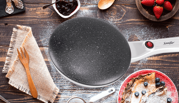 Elektrische Crêpe-Maker, antihaftbeschichtet, schwarz, auf Holztisch mit Zutaten.