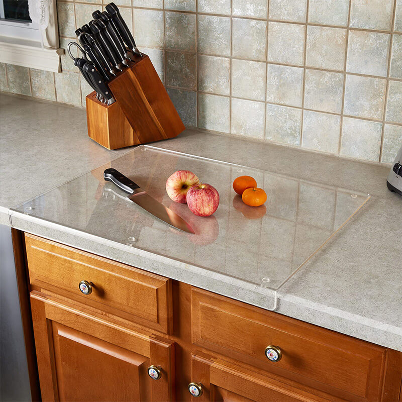 Klarglas-Schneidebrett auf Küchenarbeitsplatte mit Messer, Äpfeln und Tomaten.