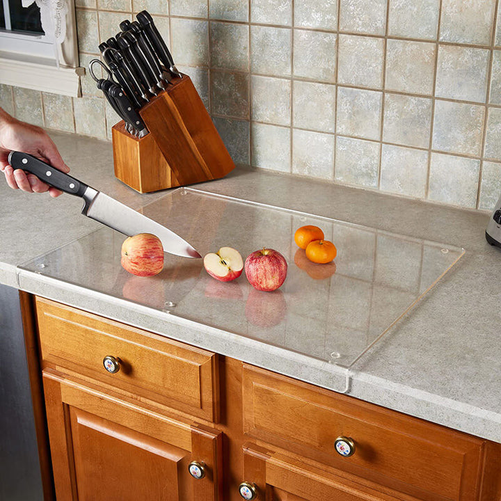 Küchenarbeitsplatte mit Glas-Schneidebrett, Messer und geschnittenen Äpfeln, moderne Küchenausstattung.