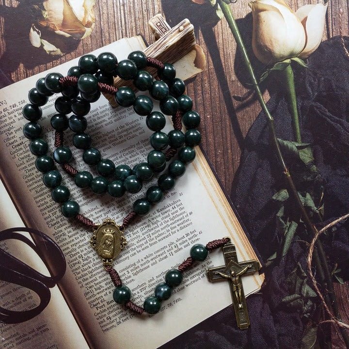 Rosenkranz aus grünen Perlen mit Kreuz auf offenem Buch, religiöses Schmuckstück, Holzuntergrund.