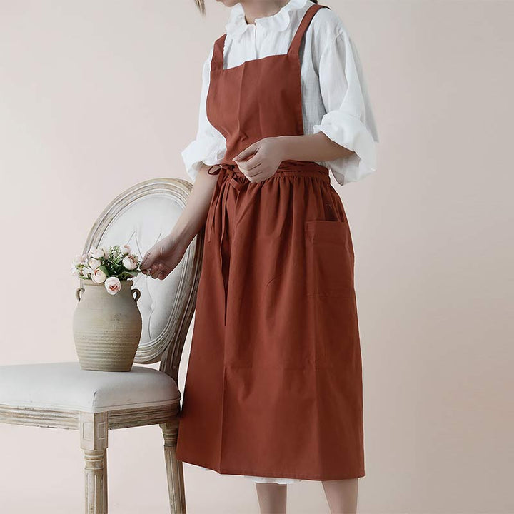Frau in brauner Schürze aus Baumwolle neben Stuhl mit Vase, Küchenschürze, modisch, praktisch.