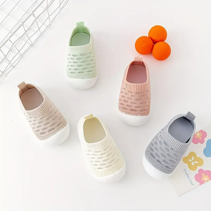 Fünf Paar Baby-Sneaker in Pastellfarben auf weißem Hintergrund mit Orangen und Blumenkarte.