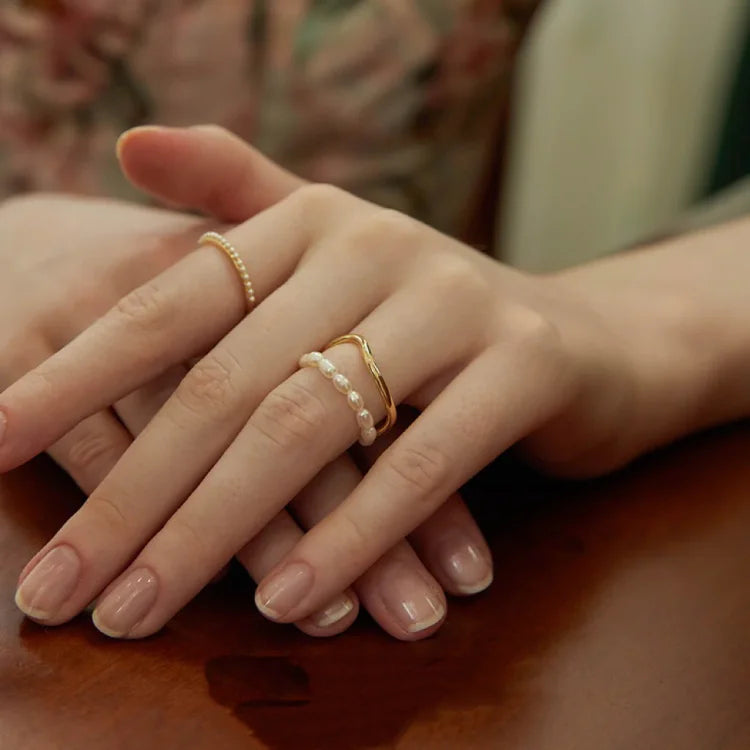 Nahaufnahme von Händen mit goldenen und perlenbesetzten Ringen auf Holztisch, eleganter Schmuck.