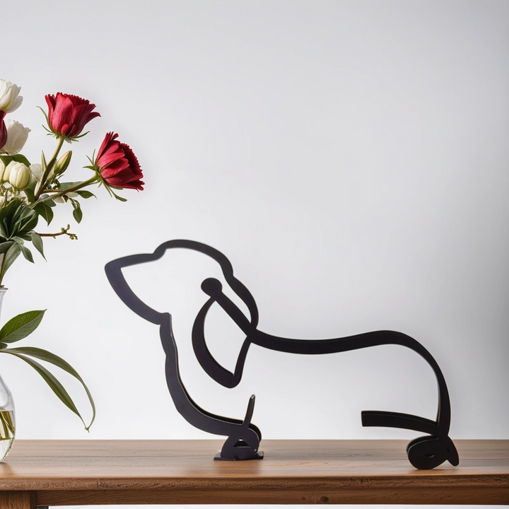 Schwarze Dackel-Skulptur aus Metall auf Holzregal neben Blumenstrauß in Vase.