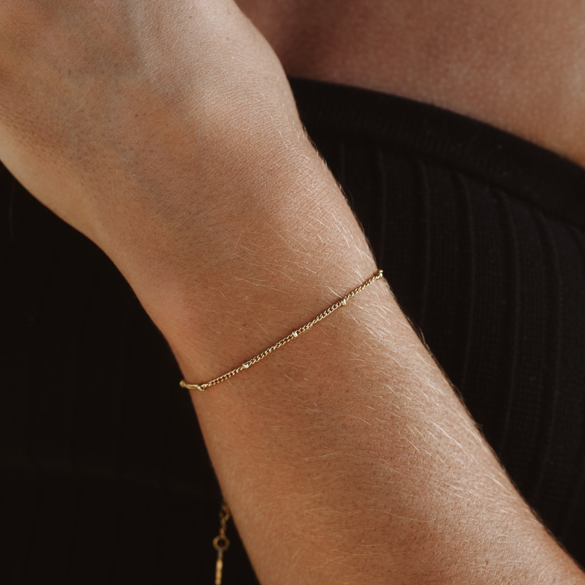 Zartes, goldenes Perlenarmband am Handgelenk, minimalistischer Schmuck, elegantes Design.