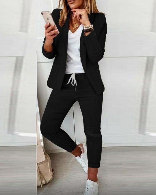 Frau in schwarzem Anzug mit weißem T-Shirt, lässiger Stil, Smartphone in der Hand.