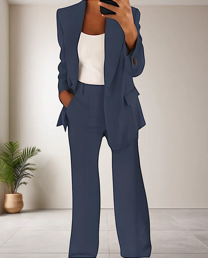 Frau im dunkelblauen Hosenanzug mit weißem Top, moderne Büroeinrichtung im Hintergrund.