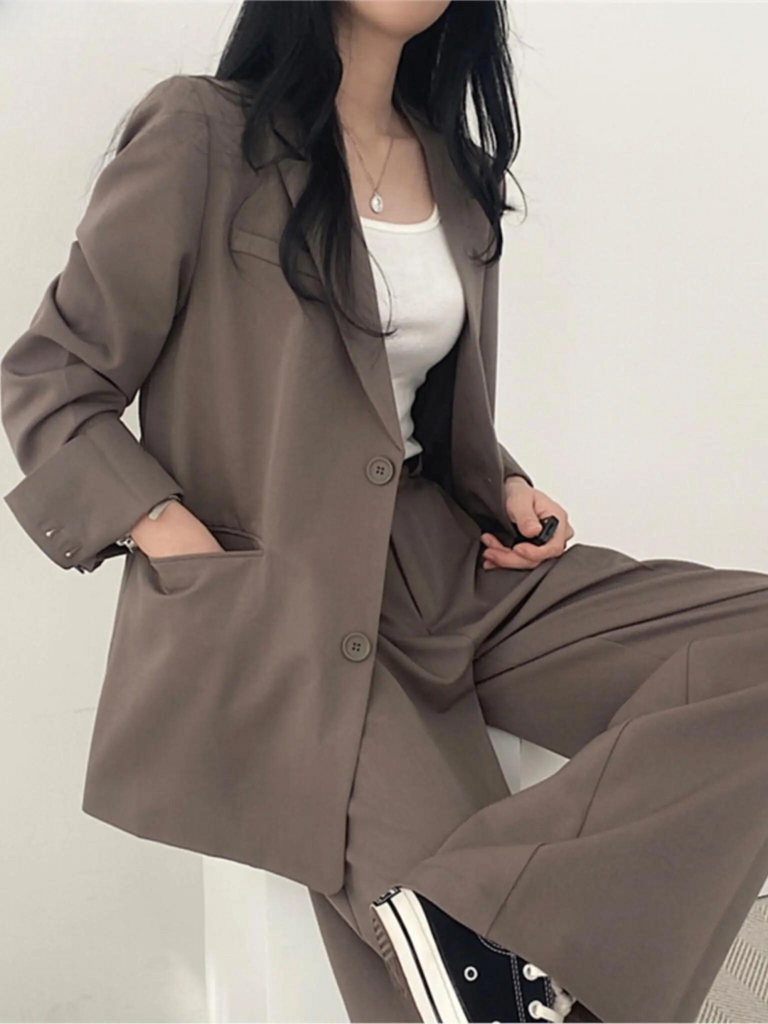 Frau in braunem Anzug mit weißem Top und schwarzen Sneakers, modisch, lässig, Business-Look.