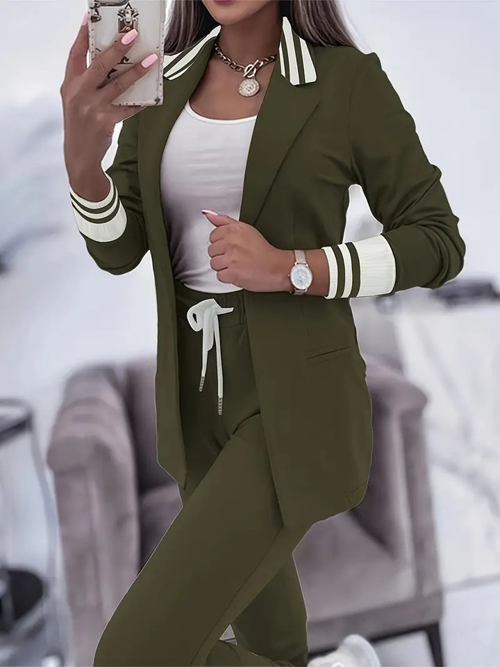Frau in olivgrünem Jogginganzug mit Blazer, weißem Top, Smartphone und Uhr im Wohnzimmer.