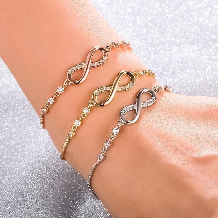 Drei Infinity-Armbänder in Gold, Silber und Roségold mit Strasssteinen auf Handgelenk.