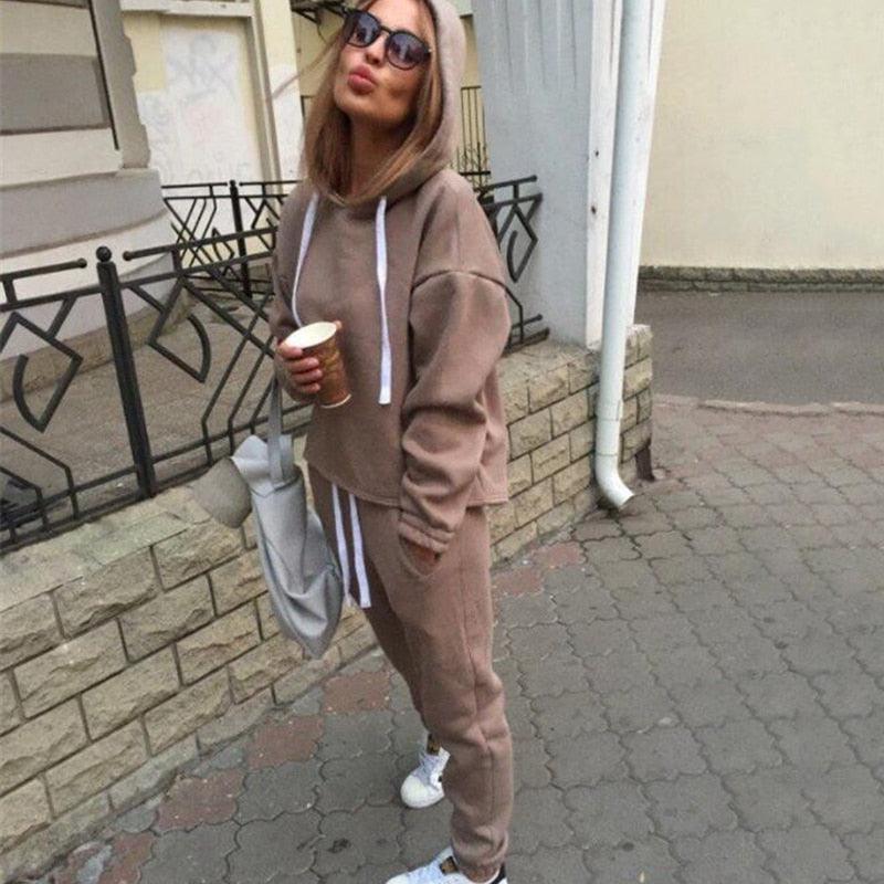 Frau in braunem Hoodie und Jogginghose, hält Kaffeebecher, lässige Straßenmode, Herbstoutfit.