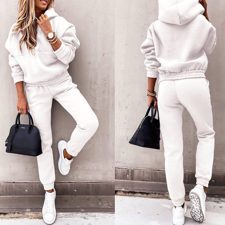 Frau in weißem Hoodie und Jogginghose, schwarze Handtasche, weiße Sneaker, lässige Mode.