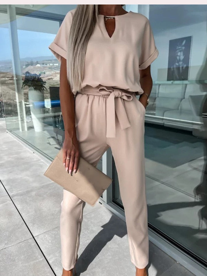 Frau in beigem Jumpsuit mit Gürtel, hält beigen Clutch, moderne Mode, eleganter Look.