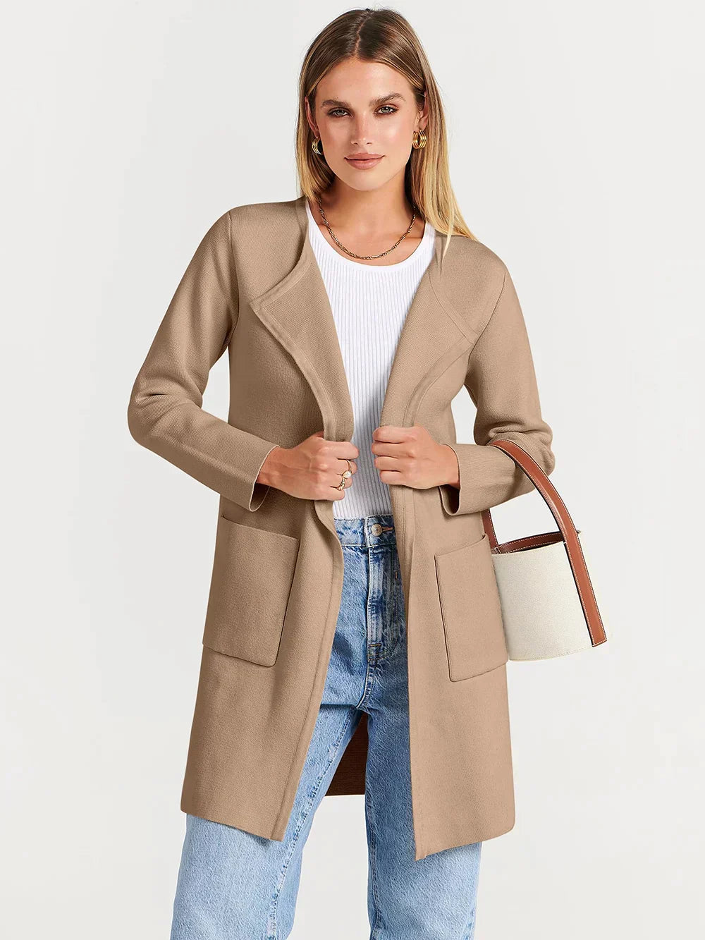 Frau in beigem Mantel, weißem Top und blauer Jeans, hält eine weiße Handtasche.