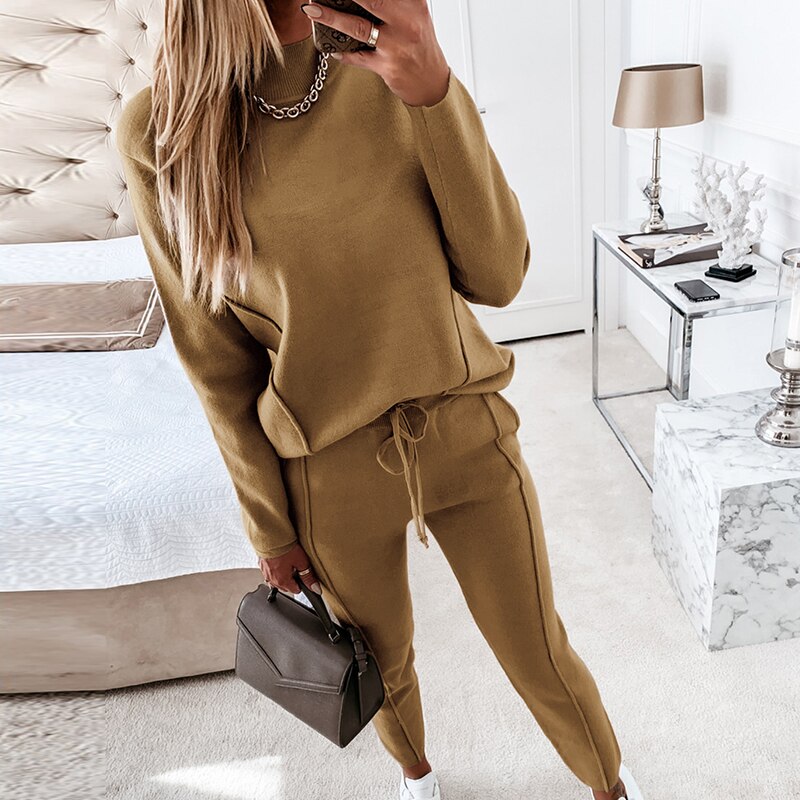 Frau in beige Strickpullover und Jogginghose, hält braune Handtasche, modernes Schlafzimmer.