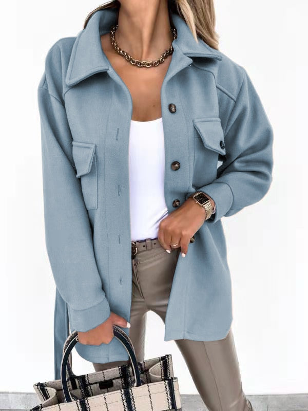 Frau in hellblauer Wolljacke, weiße Bluse, beige Hose, kariertes Handtasche, modisch elegant.