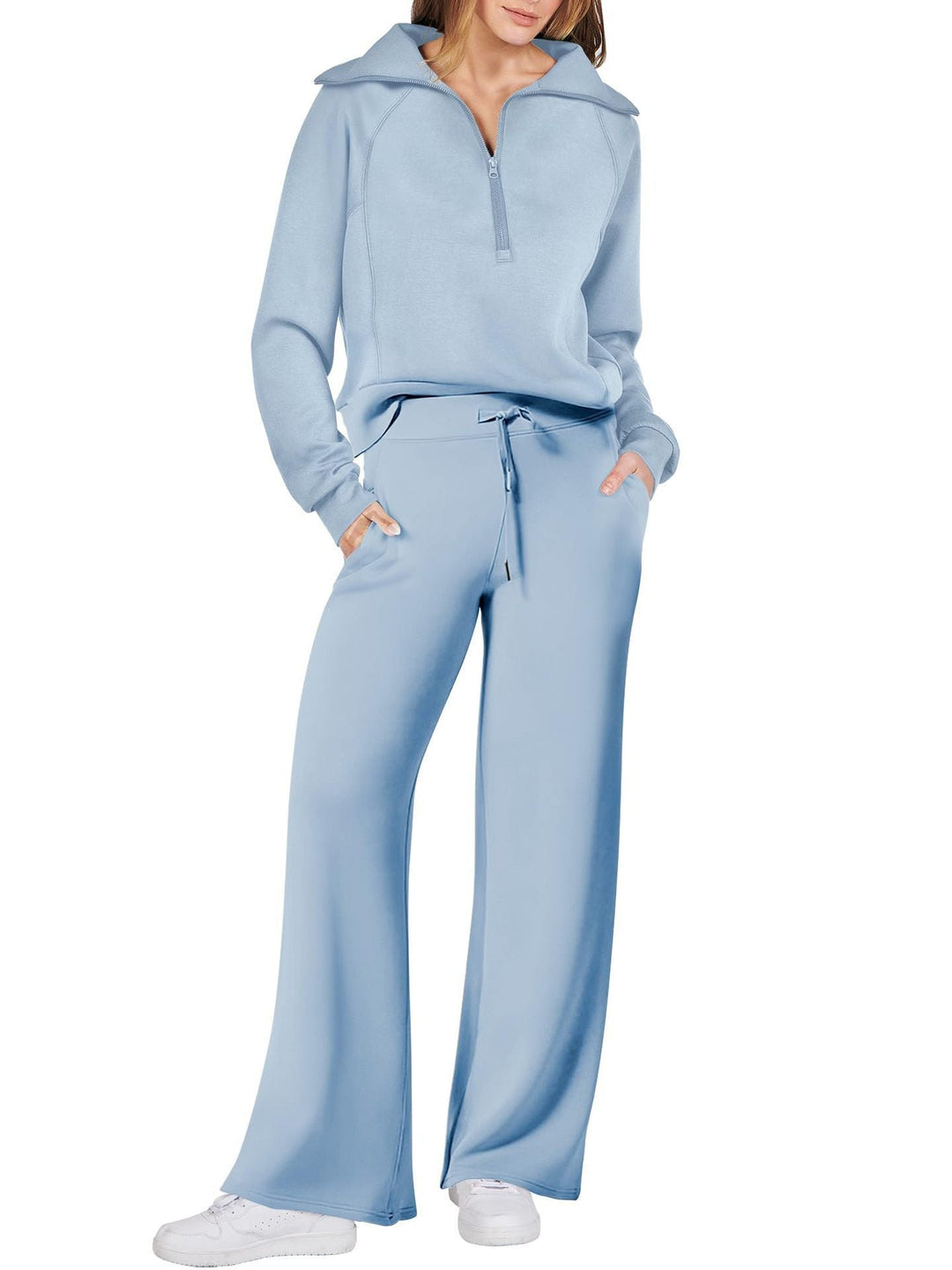 Frau in hellblauem Jogginganzug, Reißverschluss-Oberteil, weite Hose, weiße Sneaker.