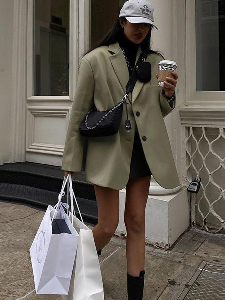 Frau in beigem Blazer mit Einkaufstaschen und Kaffeebecher, modisch, urbaner Stil.