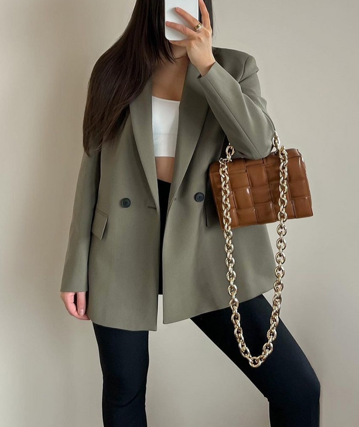 Frau in grauem Blazer mit brauner Kettentasche, weißem Top und schwarzer Hose.