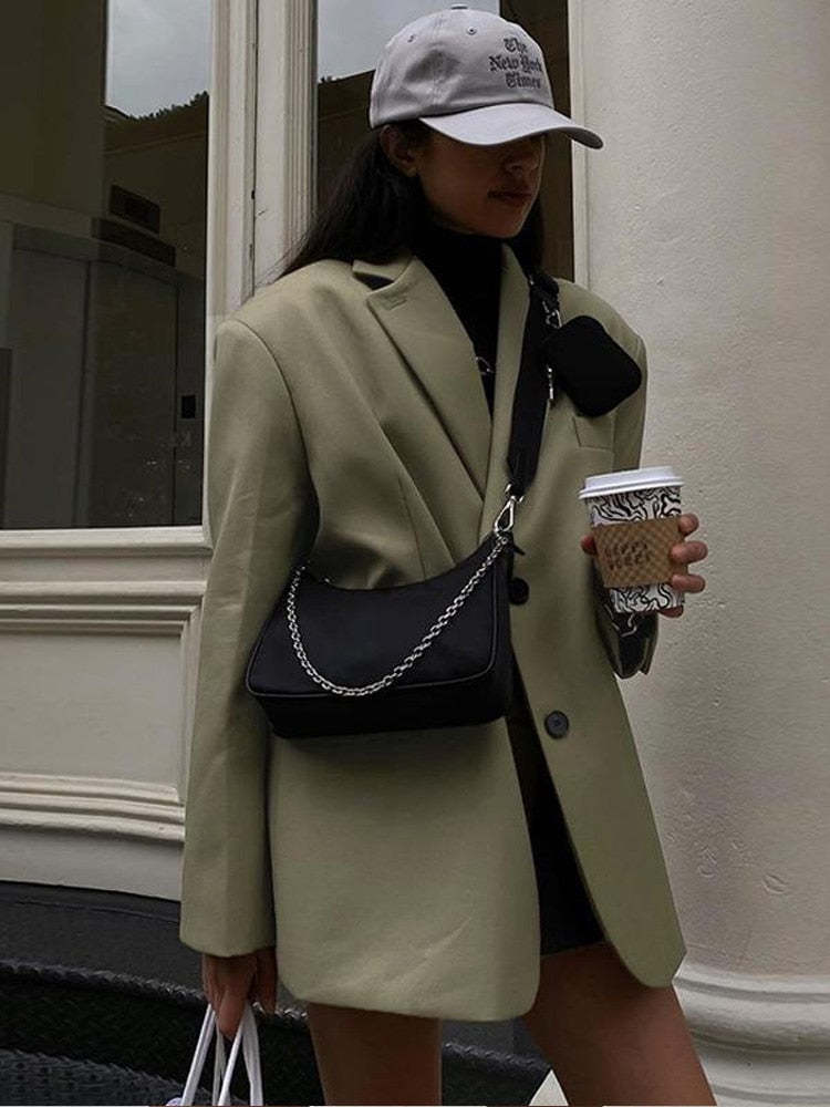 Frau in beigem Blazer mit schwarzer Umhängetasche und Kaffeebecher, modisch urbaner Stil.