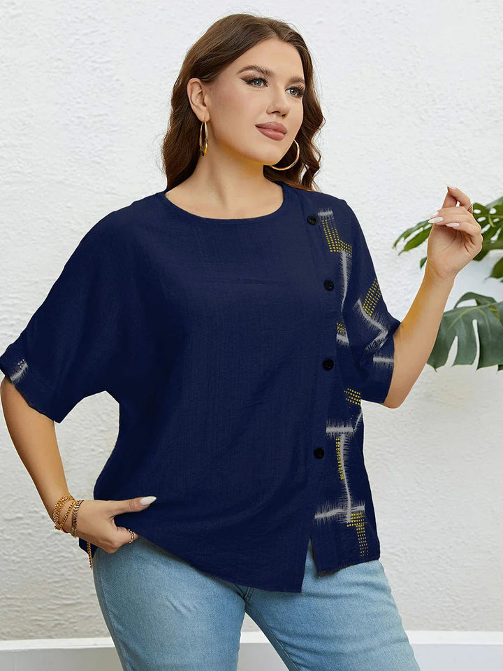 Frau in dunkelblauer Bluse mit Knöpfen und Muster, goldene Ohrringe, lässiger Look.