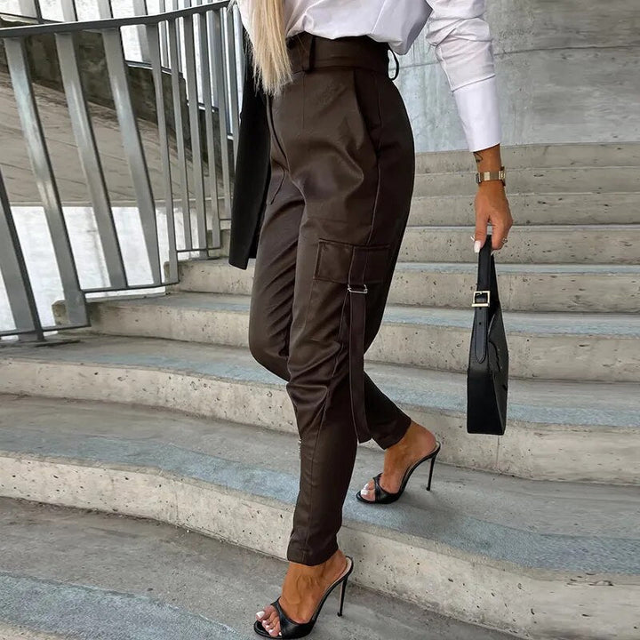 Frau in brauner Lederhose, weißer Bluse, schwarzen High Heels, schwarze Handtasche, Treppe.