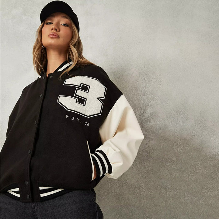 Frau in schwarzer Collegejacke mit weißer Nummer 3, Baseballkappe, lässiger Stil.
