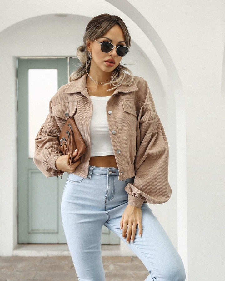 Frau in beiger Cordjacke, weißem Top, blauer Jeans, Sonnenbrille, modisch, lässig, modern.