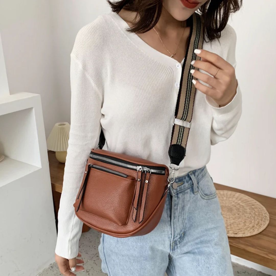 Frau mit brauner Leder-Umhängetasche, weißem Pullover und Jeans, modisches Accessoire.