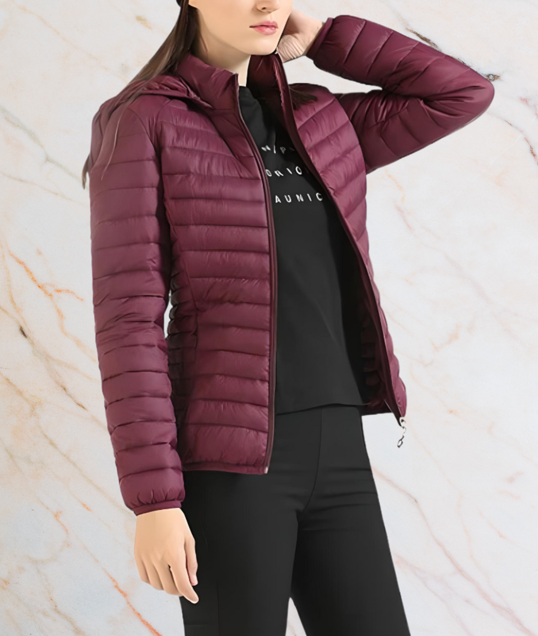 Frau in burgunderroter Daunenjacke, Reißverschluss offen, schwarze Hose, Marmorhintergrund.
