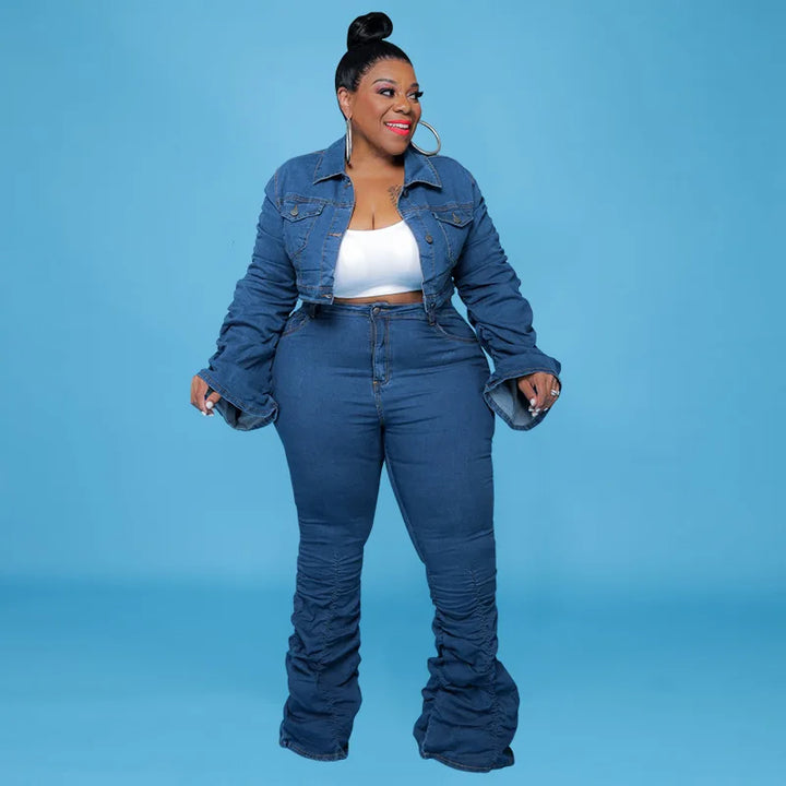 Frau in blauer Jeansjacke und Schlaghose, weißes Top, lächelnd, blauer Hintergrund.