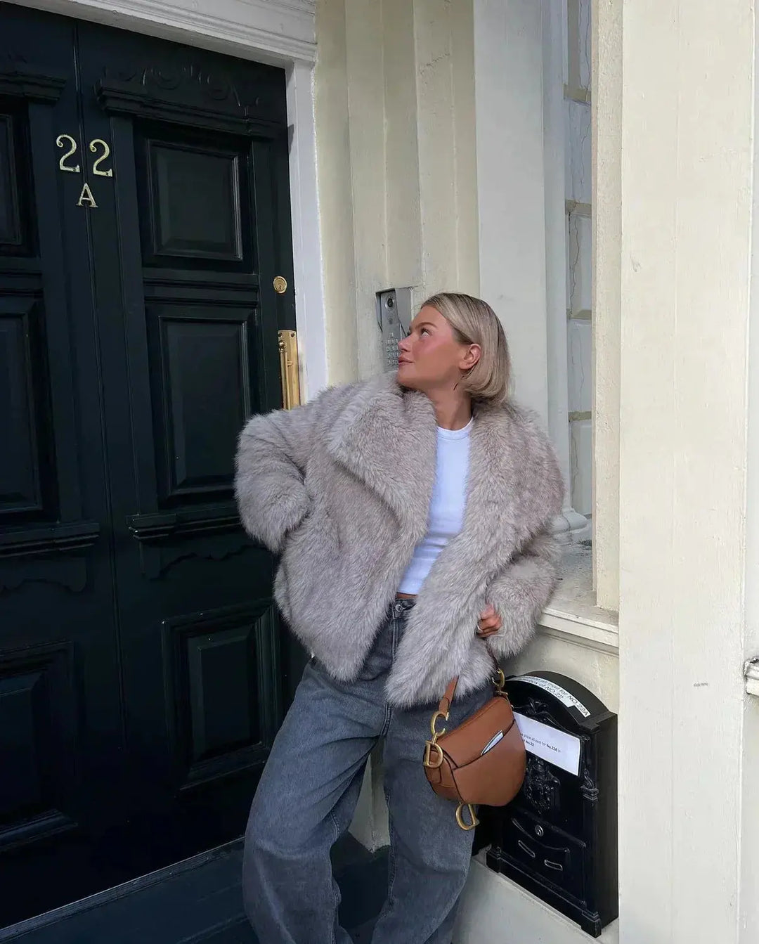Frau in grauem Kunstpelzmantel vor schwarzer Tür, modisch, urbaner Stil, Herbstmode.